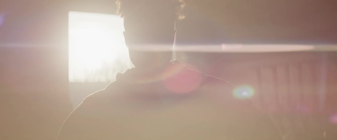 A teenage boy stands in a room as a the sun shines through the door
