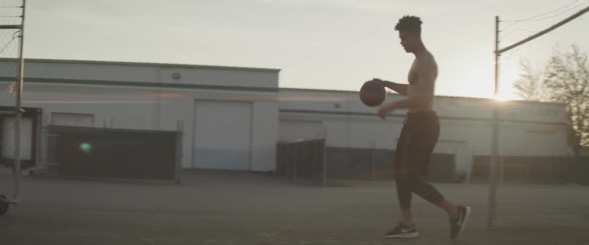A teenage boy dribbles a basketball in the evening