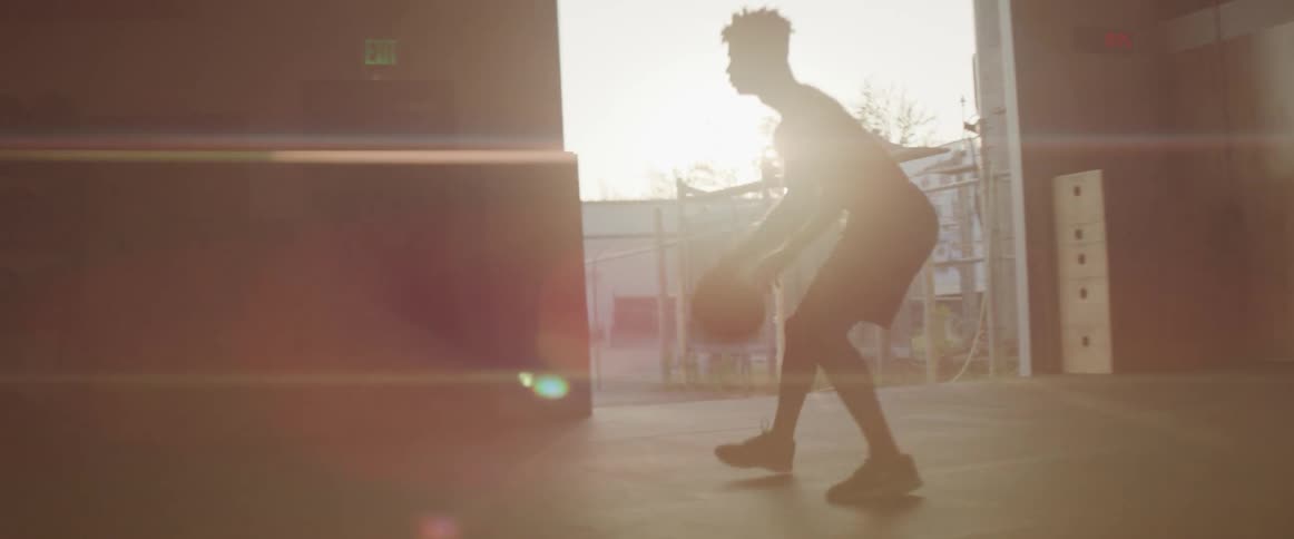 A young man dribbles a basketball inside a large room in a factory