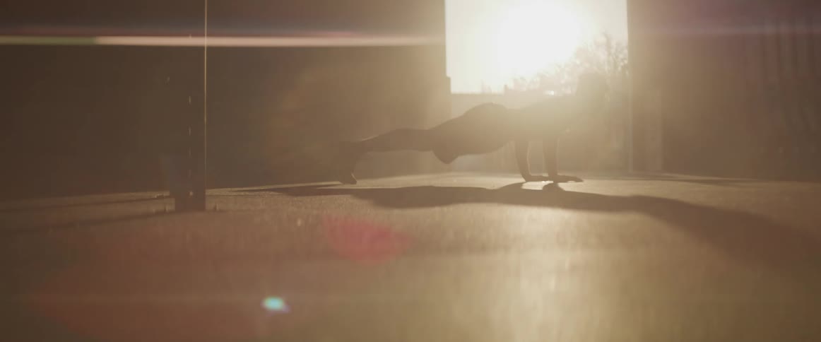 Black man doing push ups is silhouetted against the sunset
