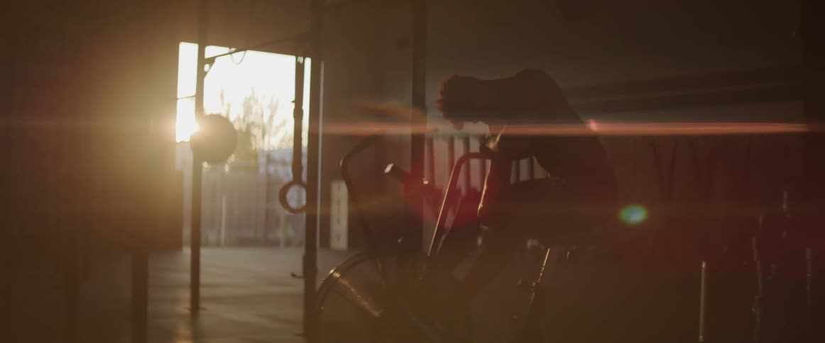 Young man sits on exercise bike in dark gym
