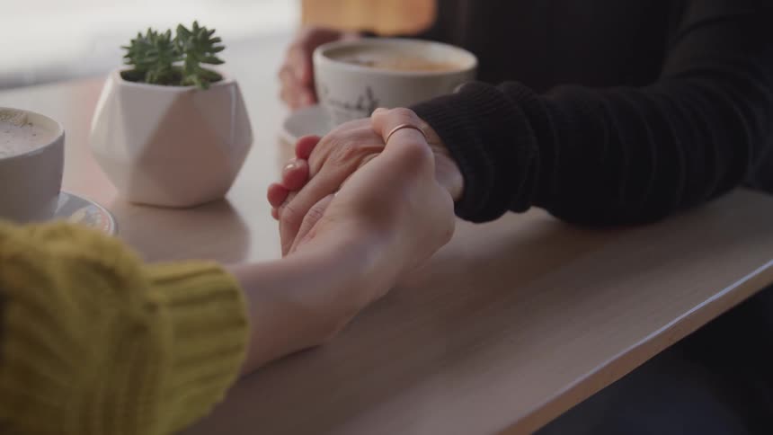 Two people in a coffee shop reach across a table and hold hands