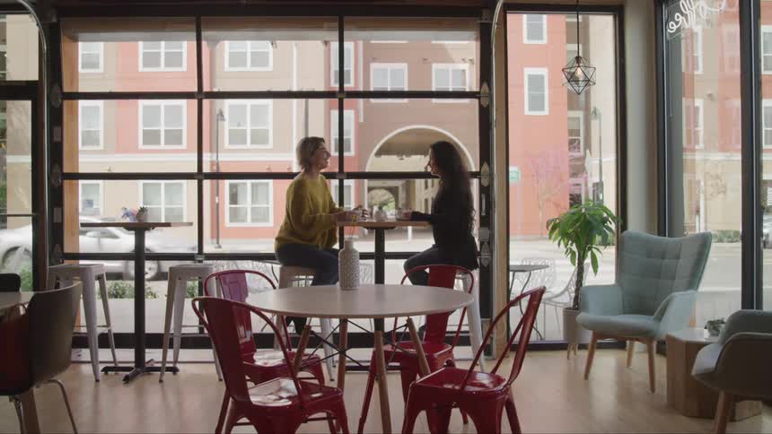 Two women sit at a table in a cafe talking together
