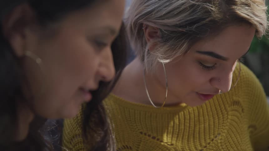 Two friends talk to each other while looking at an object out of the frame