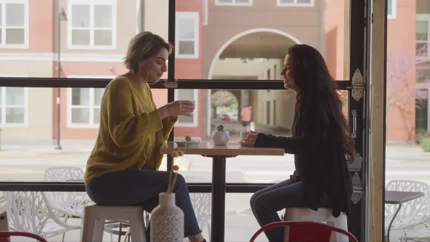 A pair of young indian women talk while drinking in a cafe during the day