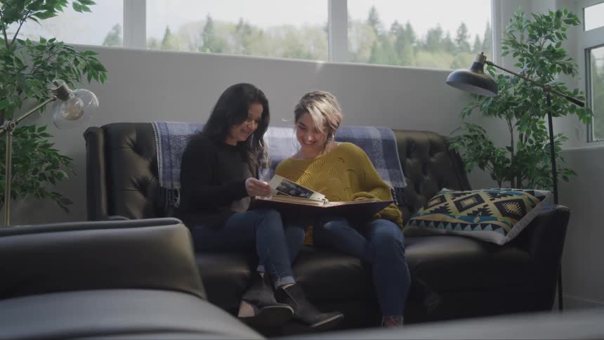 Two teenagers sit on a couch and look at a book