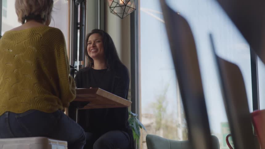 Two women sit in a restaurant together and talk and laugh