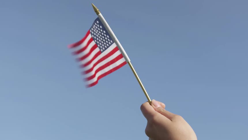 Hand holding a small american flag waving in the wind on a blue sky