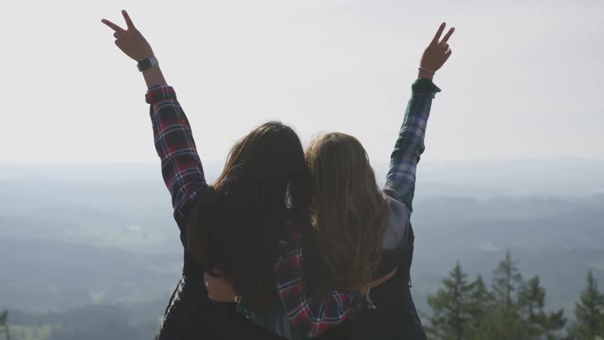 Young women with hands raised in peace signs looking out towards distant mountains