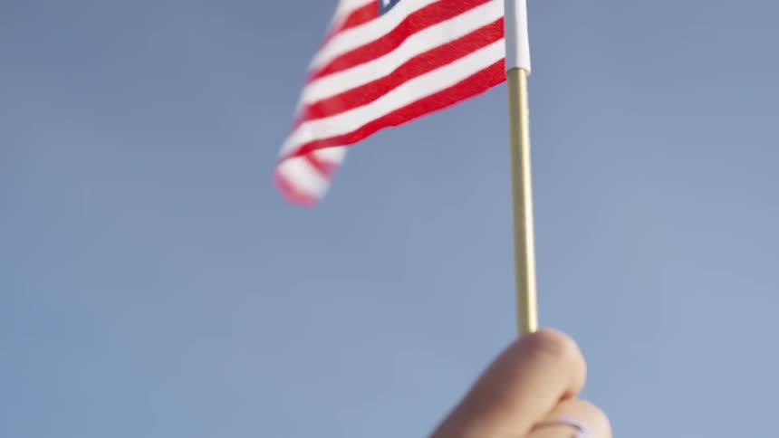 Person raises small american flag towards sky