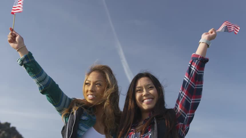 Two smiling women standing side by side holding up small american flags