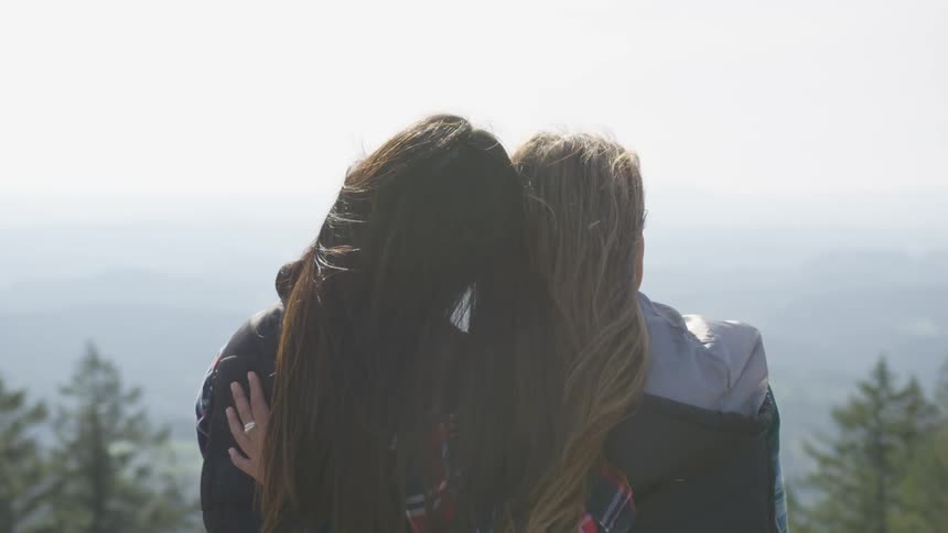 Young lesbian couple with arms around each other in front of mountain landscape