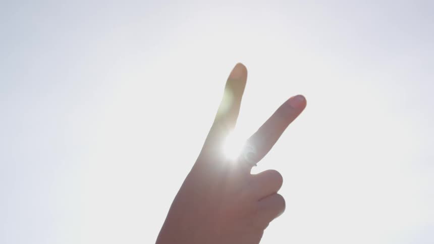Persons hand making a victory symbol is back lit by the sun