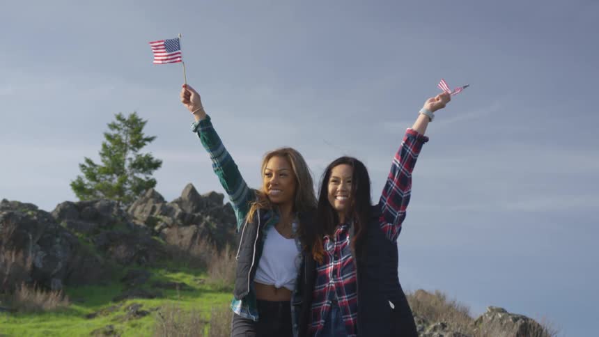 Two teenage girls hold small american flags in the air