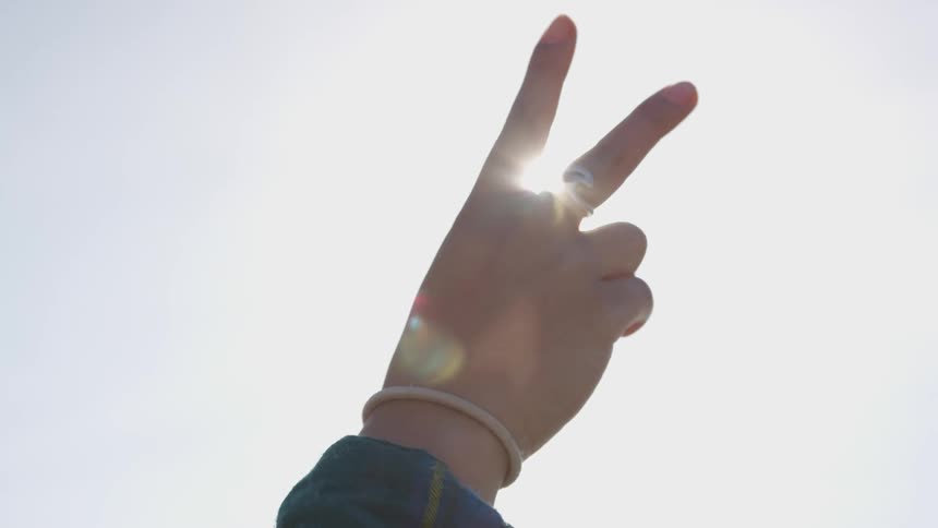 Sunlight filters through the extended fingers of a womans hand