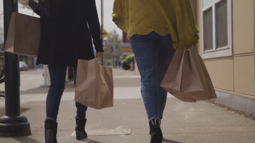 Two woman walk down a city sidewalk carrying shopping bags