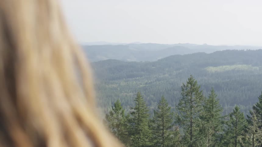 A woman is standing outdoors and looking at the forest