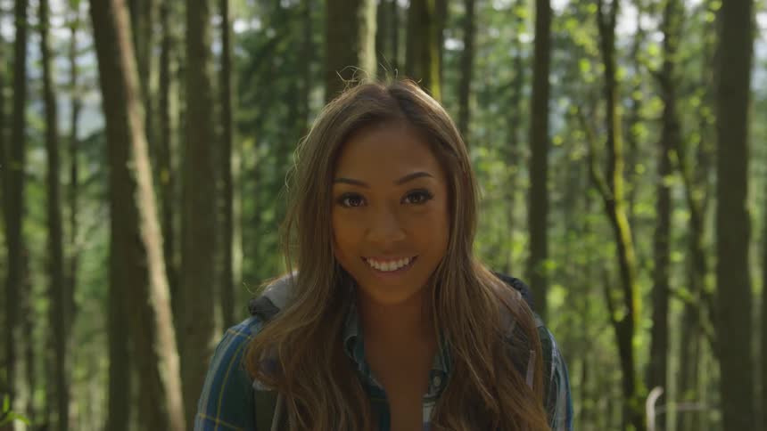 A woman is smiling outdoors in the forest