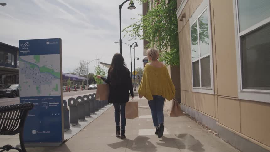 Two women walk down city street holding shopping bags