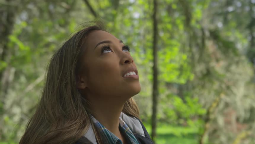 A teenage girl in a forest looks up at the trees