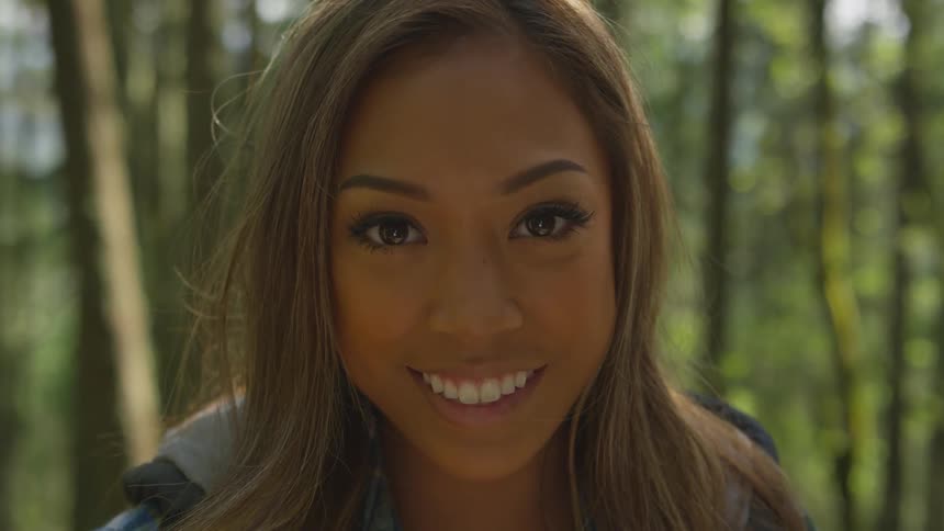 A woman is smiling outdoors in a tropical area