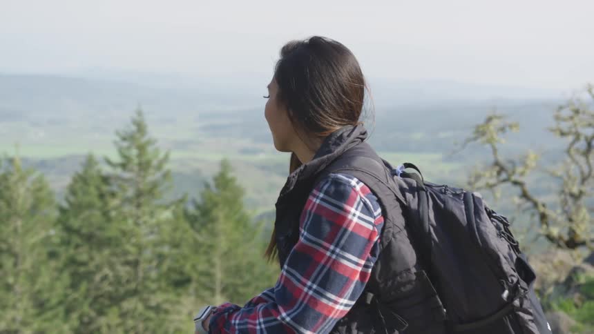 A woman is wearing a backpack and looking at a forest