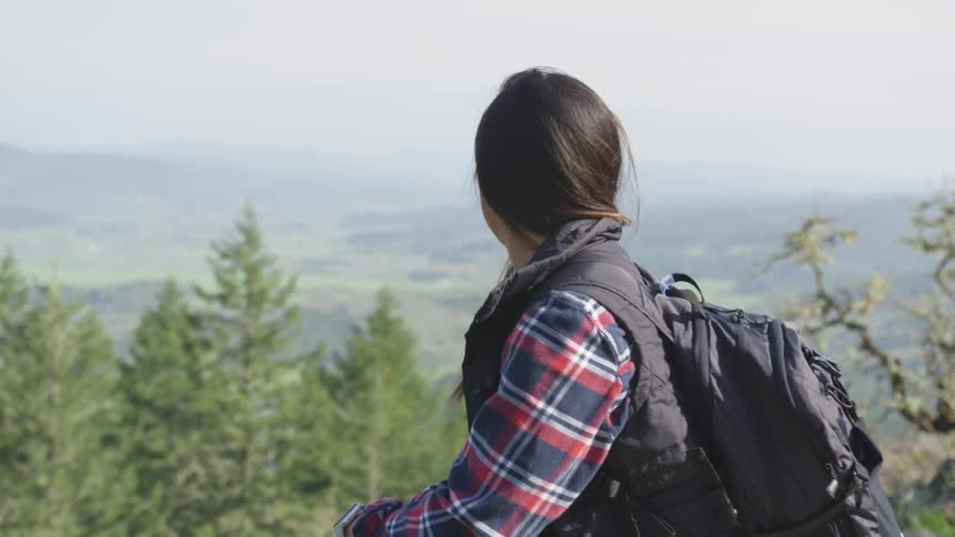 Young woman with backpack looks out over hills and mountains