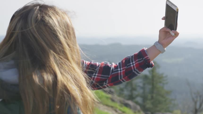 Two people take selfie standing on top of mountain over valley covered in fog