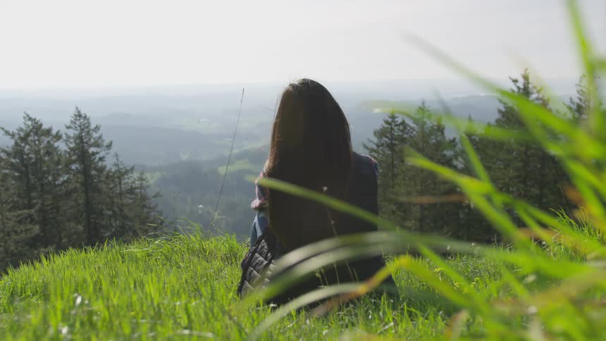 A woman sits on a hill and looks out at the landscape