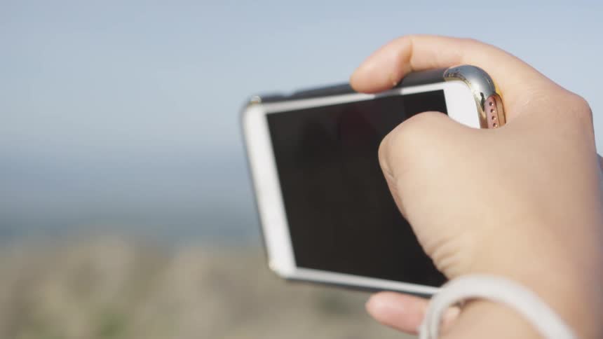 Person holds mobile phone on side facing themselves taking selfie outdoors