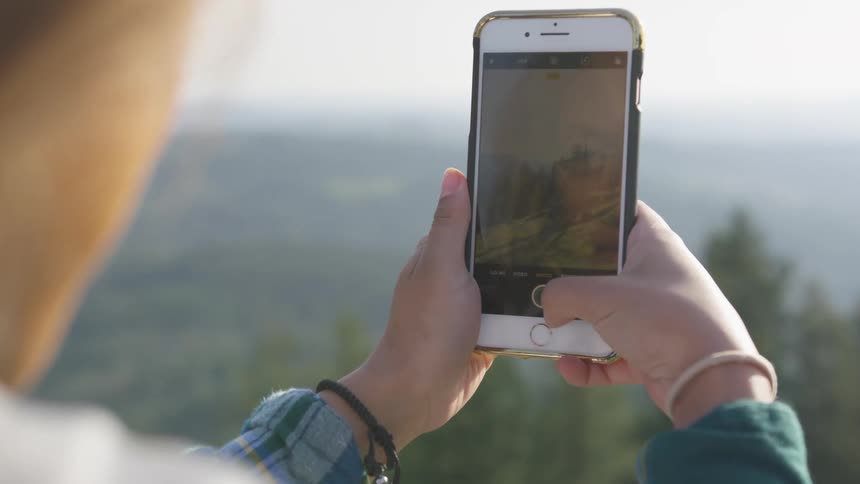 Woman takes pictures of the pine forest on the hills with her smart phone