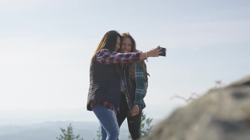 Two girls stand closely together to take a selfie while outdoors