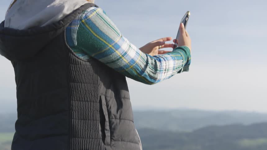 A woman takes a photo with her cell phone from the top of the mountain