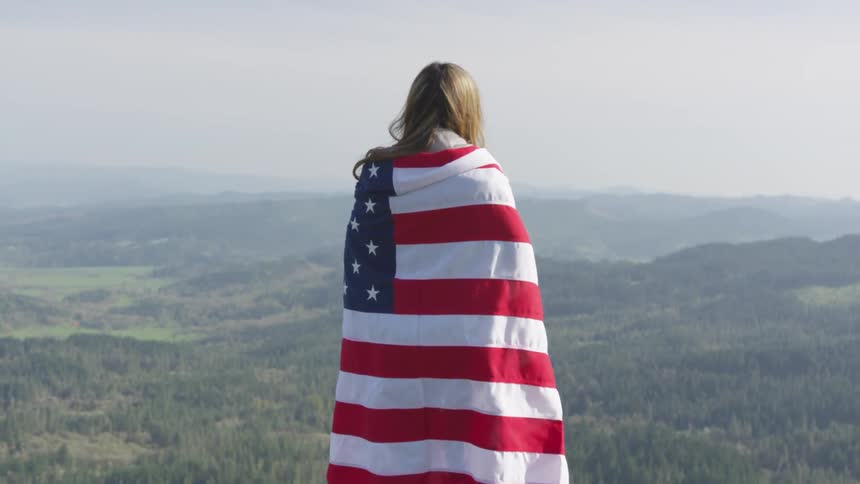 A female draped in an american flag standing near mountains