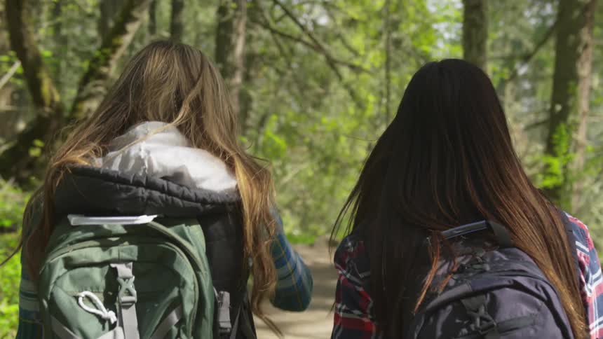 Two teenage girls walk down a path in a woodland area