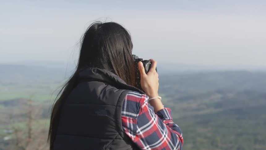 Woman atop a mountain takes pictures of the hills with a camera
