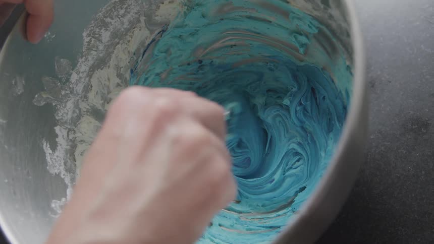 A person mixes blue paint in a bucket using a spoon