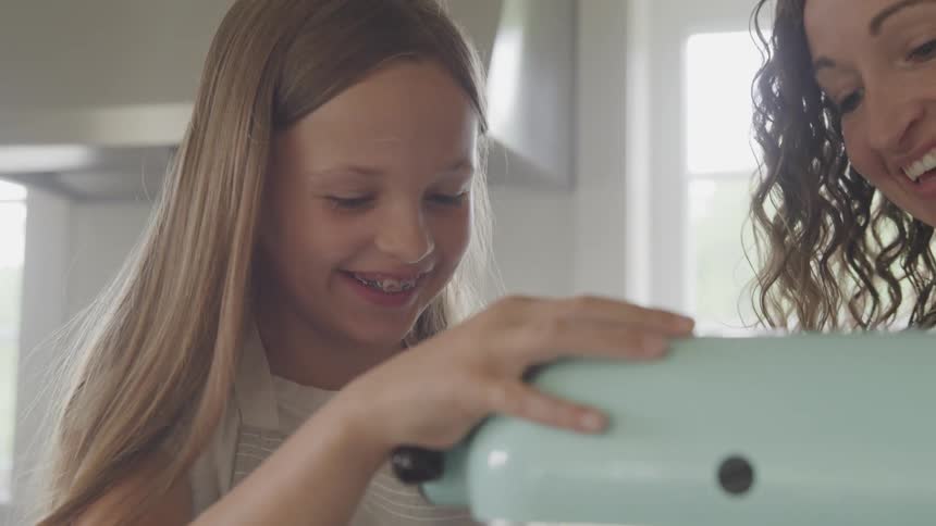 A smiling mother and daughter operate an appliance in a home kitchen during the day