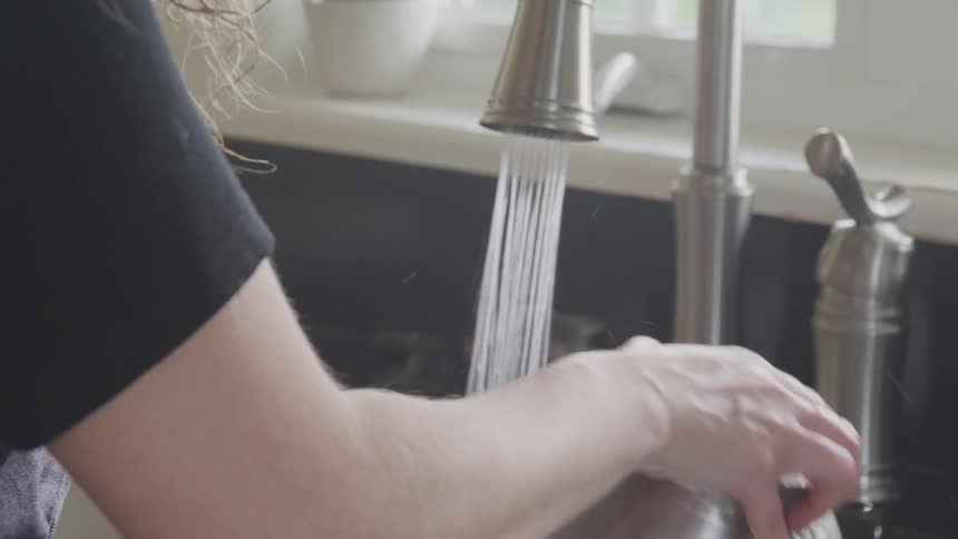 Woman washes metal mixing bowl in kitchen sink