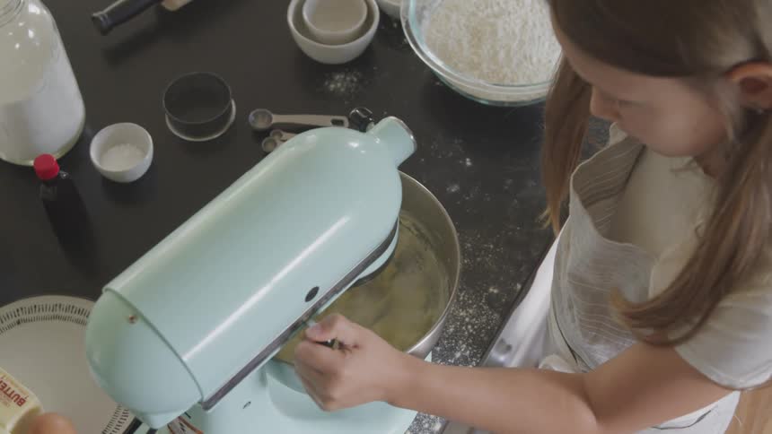 Woman wearing apron uses standing mixer on dark topped counter