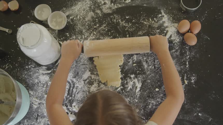 Girl rolls out dough on floured surface