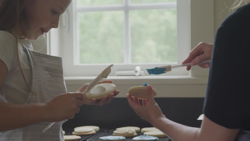 A little girl and her mom spread icing on cookies