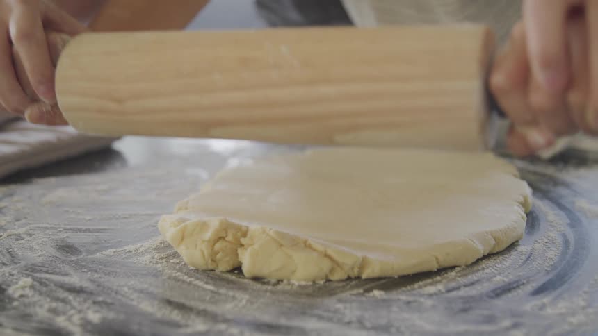 Guiding rolling pin with younger person on rolling out dough