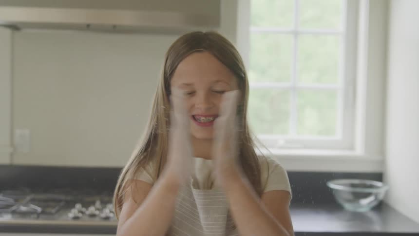 A young girl laughs as she claps her hands full of flour together