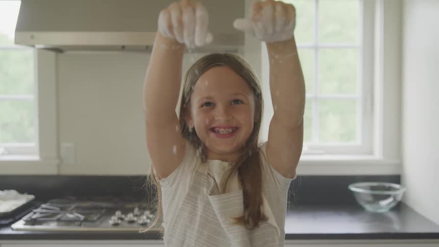 Little girl sprinkles flour from fingertips in kitchen