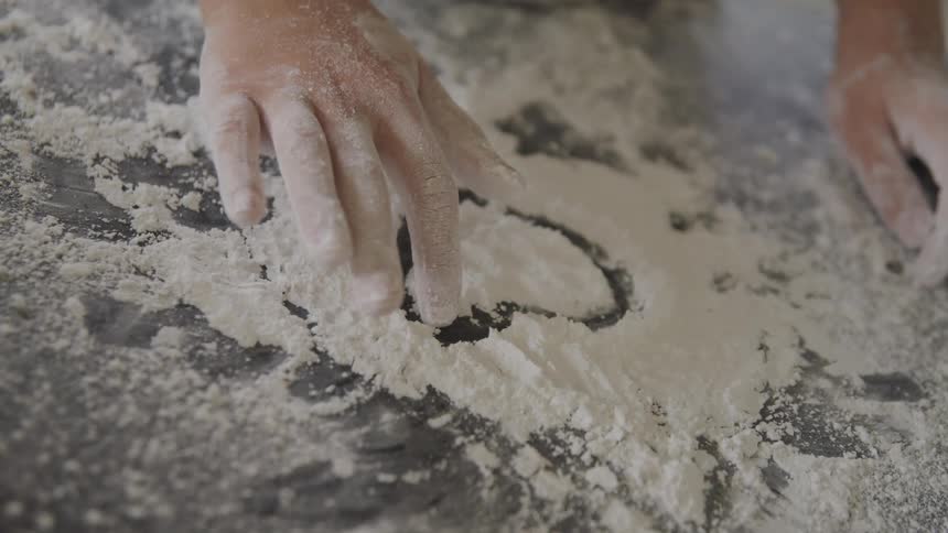A girl draws a heart in flour on a counter top at home