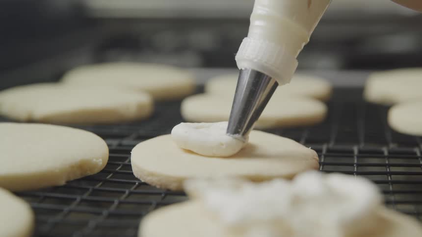 A person uses a specialized dispenser to precisely top cookies with frosting