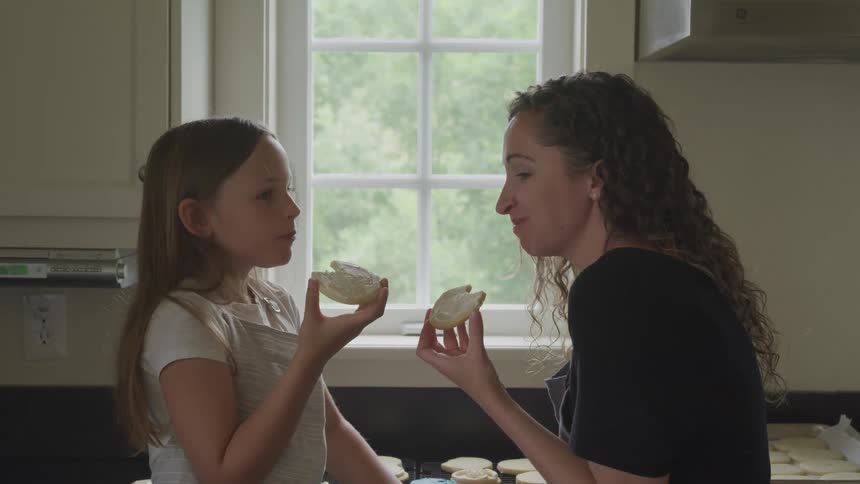 A mother and daughter eat cookies in their home kitchen