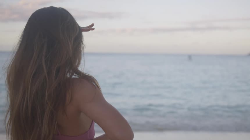 Young woman stands on the sand beach at sunset next to the ocean