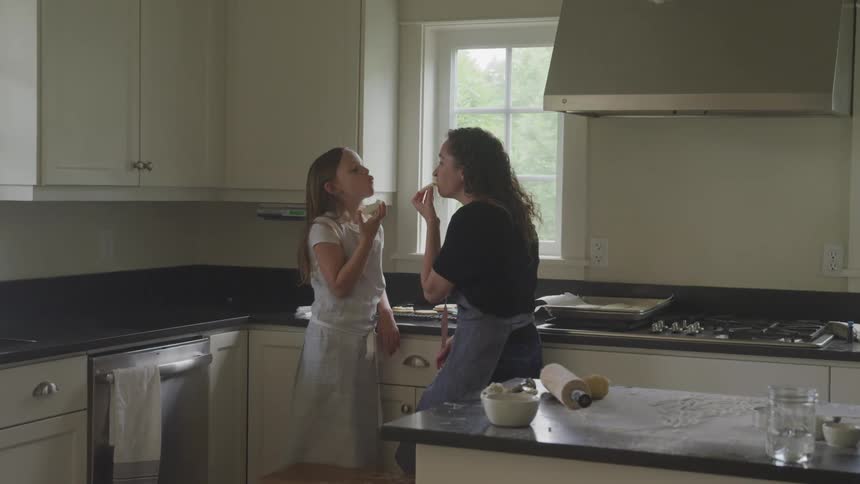 Mother and daughter eat pastry they have just baked while standing in kitchen